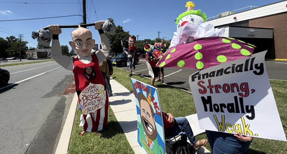 A group of people decked out in costumes by the CRI creative team are protesting against Jeff Bezos in Cherry Hill. There is a person in a Bezo costume to the right and other protestors scattered about.