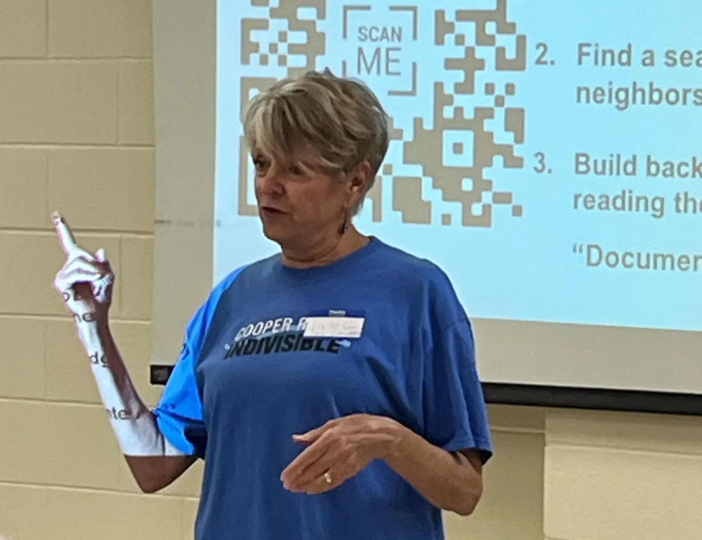 A woman in a blue shirt stand in front of a QR code as she introduces our speaker for the Rapid Response Training Day 1